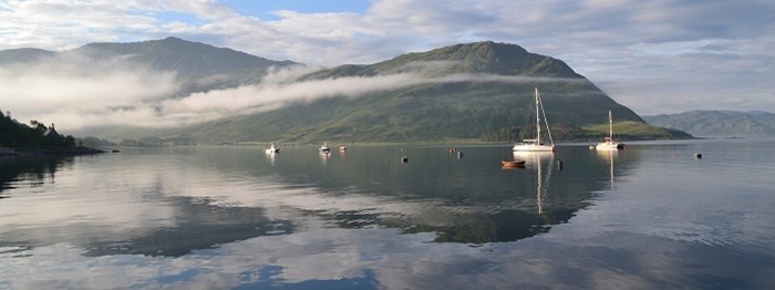 Body of water with boats on and hills covered in cloud in the background
